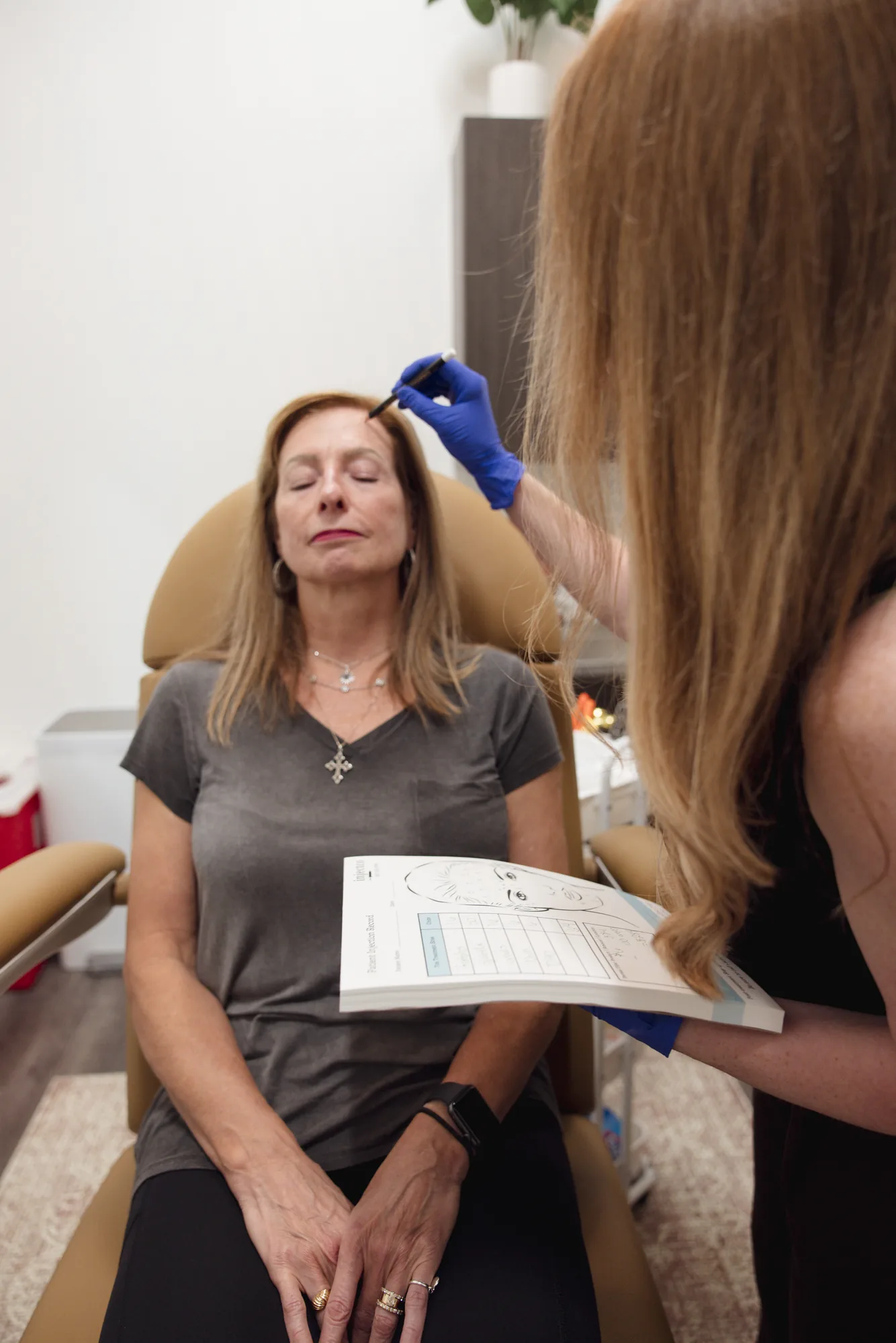 Provider marking a patient's forehead and reviewing an injection record before injectable treatment