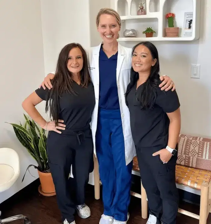 Three clinicians in scrubs standing together in a treatment room.