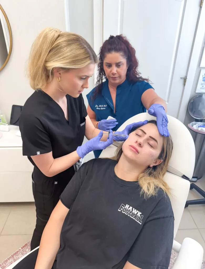 A course participant injecting a mapped treatment area on a live model while an instructor supports the model's head and observes closely.