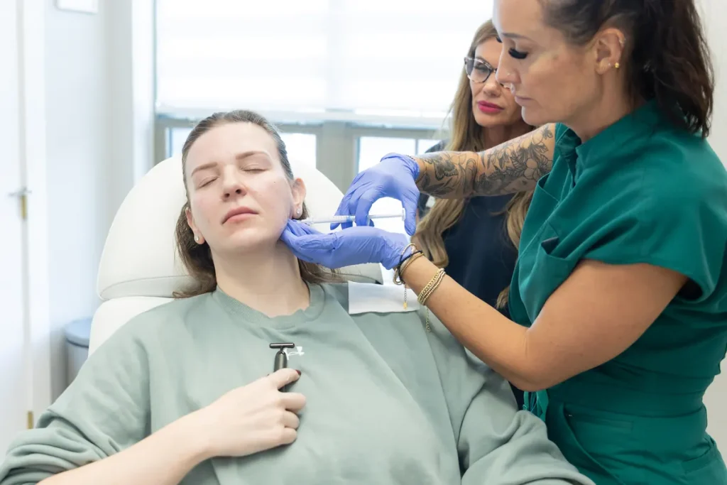 A clinician injecting along a model's jawline while a second clinician observes the angle of approach.