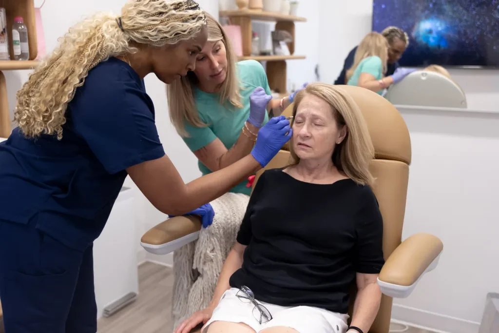 Two clinicians working with a seated model in a training room while a second pair works in the background.