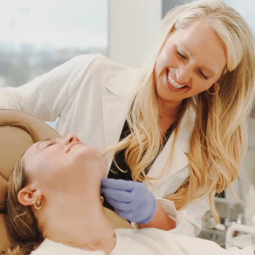 Provider in a white coat gently examining a reclined client's neck during a skin treatment